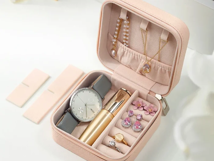 Et lyserødt smykkeskrin med et armbåndsur, læbestift, halskæder, en ring, øreringe og et armbånd, alt sammen pænt organiseret indeni.