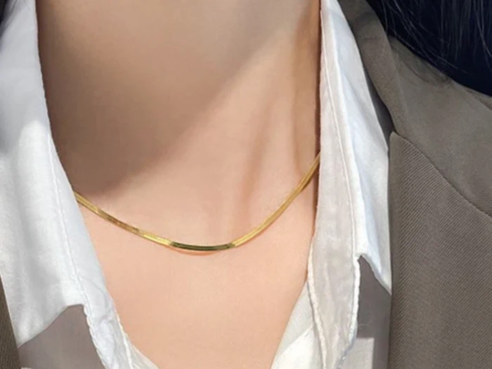 En person iført en guldhalskæde, en hvid skjorte med krave og en grå blazer.