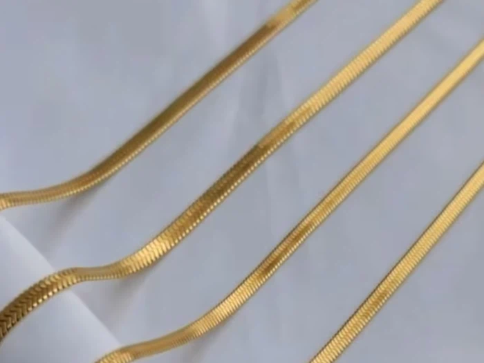 Fire guldkæder er lagt diagonalt på en hvid stofbaggrund, og hver kæde reflekterer lyset og viser et fladt, glat design.