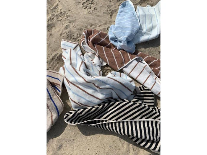 Flere stribede håndklæder i blå, brune og sorte nuancer er spredt ud og krøllet sammen på sandstranden.