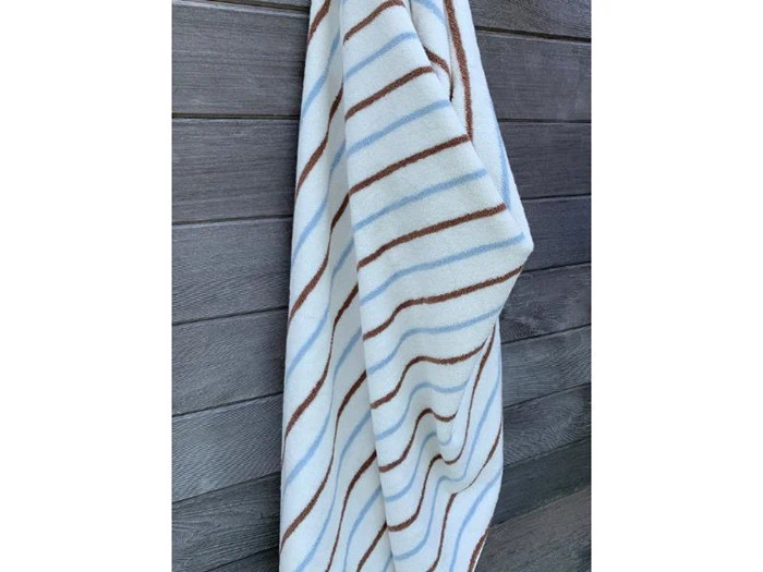 Et hvidt håndklæde med lyseblå og brune striber hænger på en mørk trævæg.