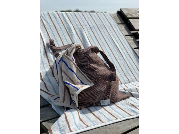 En brunstribet taske og et håndklæde med blå og brune linjer hviler på en træstol i solen.