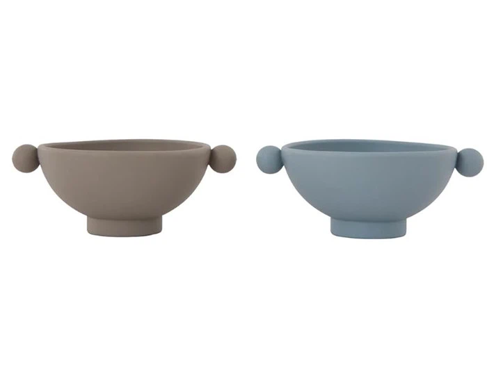 To silikoneskåle med sidehåndtag, en taupe og en lyseblå, hver med et lille håndtag på den modsatte side, på en hvid baggrund.