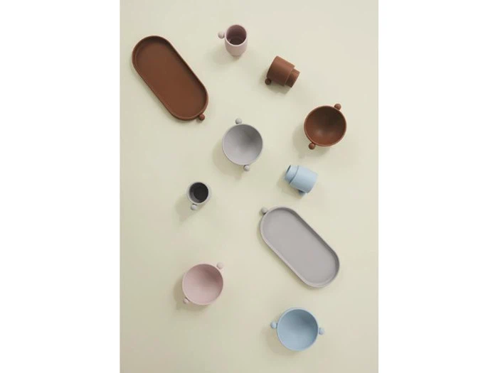 Forskellige pastelfarvede kopper og bakker arrangeret i et spredt mønster på en lys beige baggrund, set ovenfra.