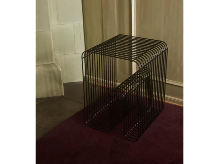 Et moderne sort wireframe-sidebord med en rektangulær form, placeret på et mørklilla tæppe nær en beige væg og et hjørne.