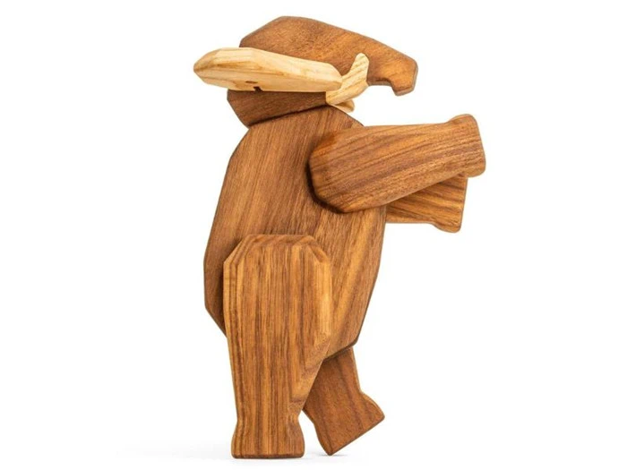 En træfigur af en bjørn med hat, der står oprejst med det ene ben løftet og den ene arm strakt frem.