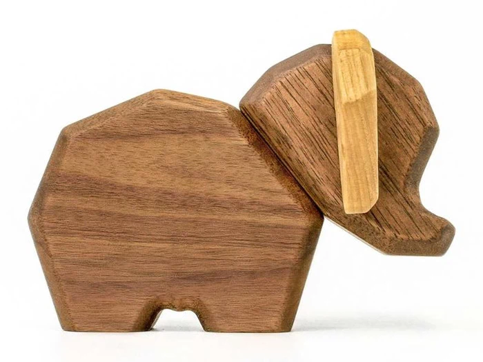 En minimalistisk elefantfigur i træ med en geometrisk krop og en lysere stødtand på en almindelig hvid baggrund.