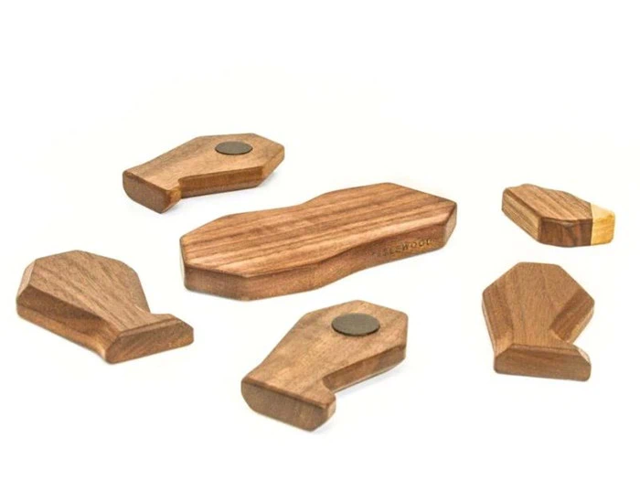 Seks geometriske træstykker, nogle med magneter, er anbragt på en hvid baggrund. Brikkerne varierer i form og størrelse, med en kisteformet brik i midten.
