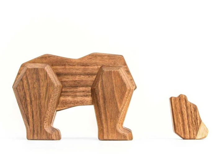 To minimalistiske, geometriske dyrefigurer i træ, en stor og en lille, der ligner en bjørn og dens unge, står på en hvid baggrund.