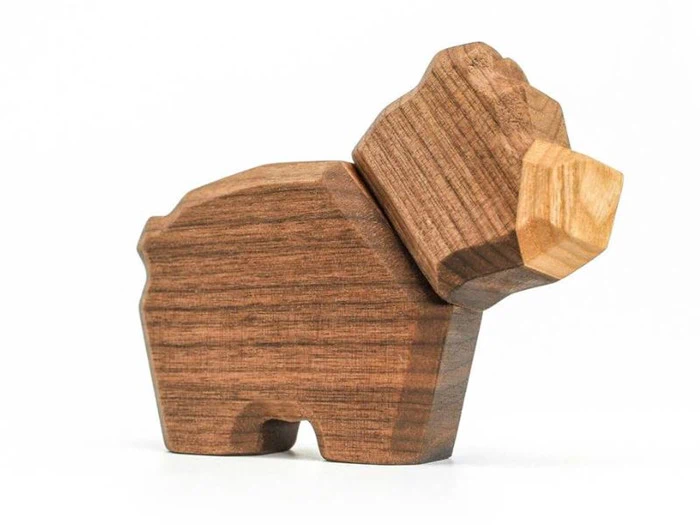 En legetøjsfigur af træ formet som en bjørn med et facetteret design og en lys snude, der vises på en almindelig hvid baggrund.