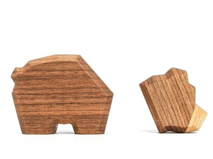To enkle dyrefigurer af træ, den ene ligner en bjørn og den anden en sten eller et mindre dyr, begge lavet af lysebrunt træ, placeret på en hvid baggrund.