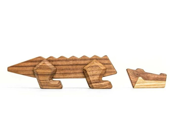 To legetøjskrokodiller af træ, en stor og en lille, begge med enkle, geometriske former og naturlige træårer, placeret på en hvid baggrund.