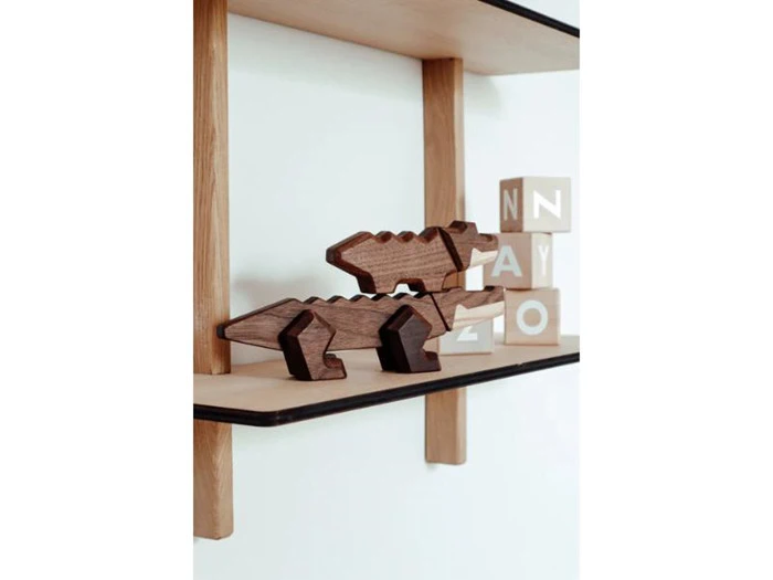To krokodillefigurer af træ er stablet på en hylde. Bag dem er der fire træklodser med bogstaver på en hvid baggrund.