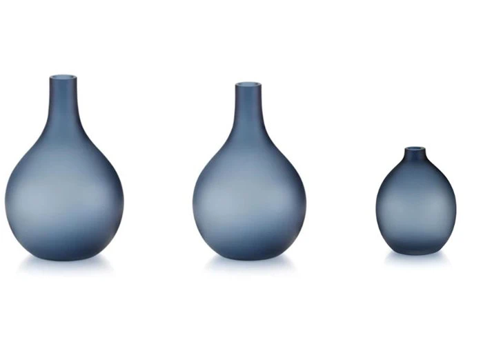 Tre blå, matterede glasvaser i forskellige størrelser står på række på en hvid baggrund.