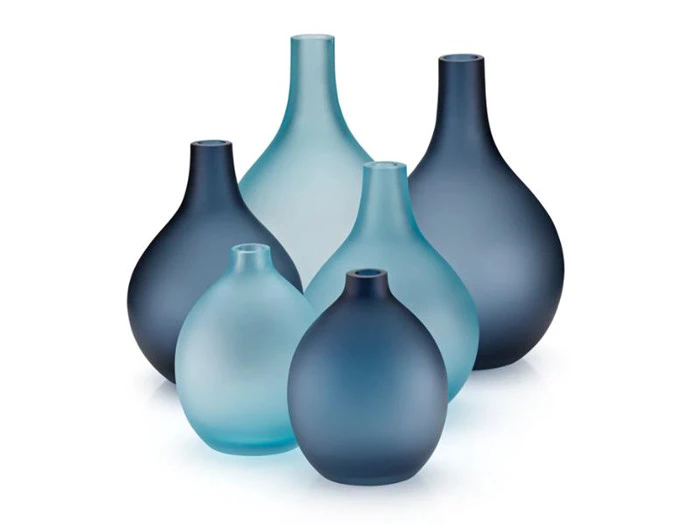Seks matte glasvaser i forskellige blå nuancer er arrangeret sammen mod en hvid baggrund. Hver vase har en afrundet krop med en smal hals.