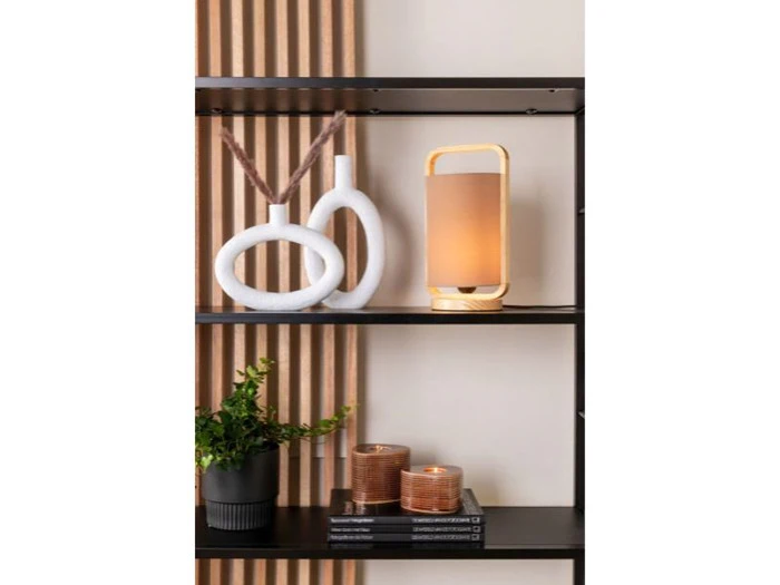 På en sort hylde står to hvide vaser med sløjfe, en moderne lampe, en lille potteplante, to stearinlys og en stak bøger op ad en beige væg med lodrette trælameller.