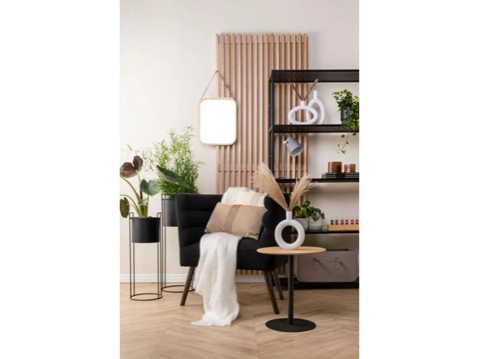 Et moderne opholdsrum med en sort lænestol, neutrale puder, planter, et lille rundt bord, dekorative hylder og et vægspejl over trælameller.