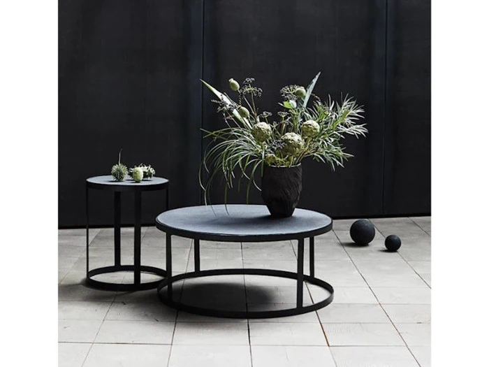 To runde, sorte metalborde på et flisegulv; på det store bord står en vase med høje, grønne planter, mens der på det lille står små sukkulenter i potter. To sorte kugler står på gulvet.