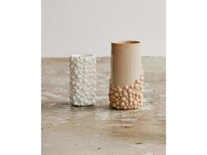 To teksturerede keramikvaser står på et betongulv; den venstre vase er lille og hvid, mens den højre vase er højere, halvt beige og halvt tekstureret beige.