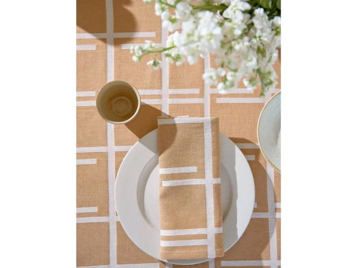 En hvid tallerken med en beige og hvid geometrisk serviet, en kop og hvide blomster på en matchende mønstret dug.