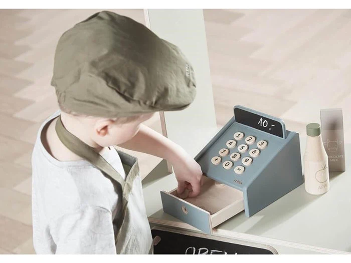 Et lille barn med kasket leger med et legetøjskasseapparat og åbner skuffen. Flasker og emballage er synlige på disken.