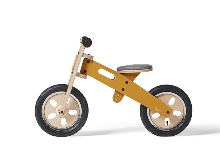 Gul løbecykel i træ med sorte dæk og et mørkt sæde, vist i profil på en hvid baggrund.