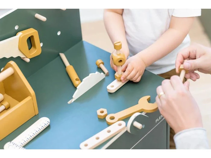 Et barn og en voksen leger med legetøjsværktøj i træ, bl.a. en sav, en skruenøgle, en lineal og skruer, på et blåt legearbejdsbord.