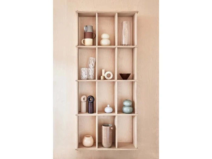 En væghængt træhylde med tolv rum, der hver især rummer forskellige minimalistiske keramikvaser, kopper og pyntegenstande i neutrale toner.