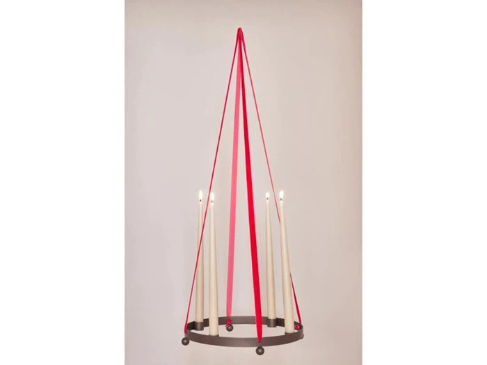 En cirkulær sort lysestage med fire tændte hvide lys, der hænger ned fra loftet i røde bånd i en minimalistisk stil.