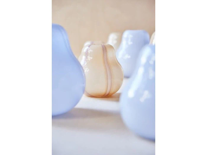 En gruppe pæreformede glasgenstande, de fleste lyseblå, med en central beige glaspære i fokus mod en neutral baggrund.