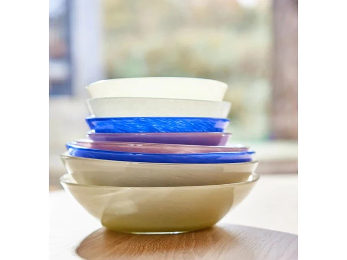 En stak farverige skåle, bl.a. cremefarvede, blå og lilla, står på en træoverflade med en sløret baggrund.