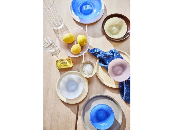 Farverige glasskåle, citroner, smør, et blåternet klæde, to glas og en skål med salt står på et lyst træbord.