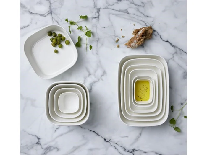 Hvide skåle på en marmoroverflade, nogle med grønne oliven, olivenolie, ingefærrod og frisk koriander spredt rundt omkring.