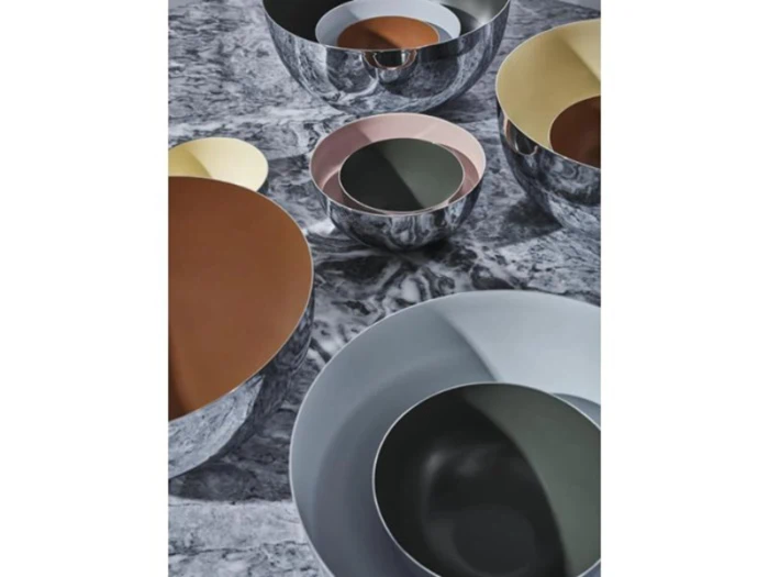 Flere reflekterende skåle med farverigt, overlappende interiør i nuancer af brun, guld, pink, grøn og grå er arrangeret på en marmoreret overflade.