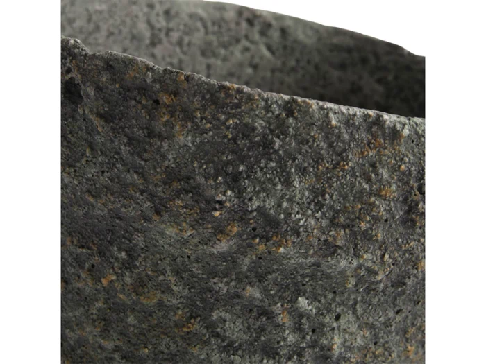 Nærbillede af en ru, struktureret, mørkegrå stenoverflade med en ujævn kant, muligvis kanten af en stenpotte eller et kar.