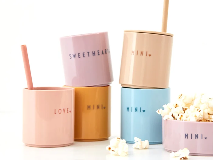 Fem pastelfarvede krus med forskellige ord som SWEETHEART, MINI og LOVE, med popcorn, der vælter ud af det ene krus i forgrunden.