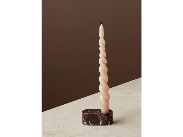 Et højt, lyserødt, snoet lys står oprejst i en mørkebrun marmorholder på en lys flade mod en brun baggrund.