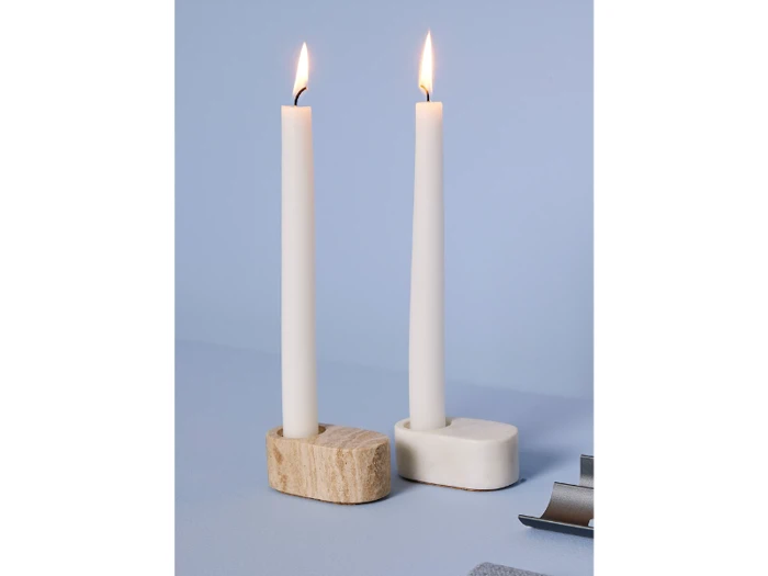 To tændte hvide bloklys i enkle stager - en i beige sten, en i hvid - på en lyseblå flade med minimalistisk baggrund.