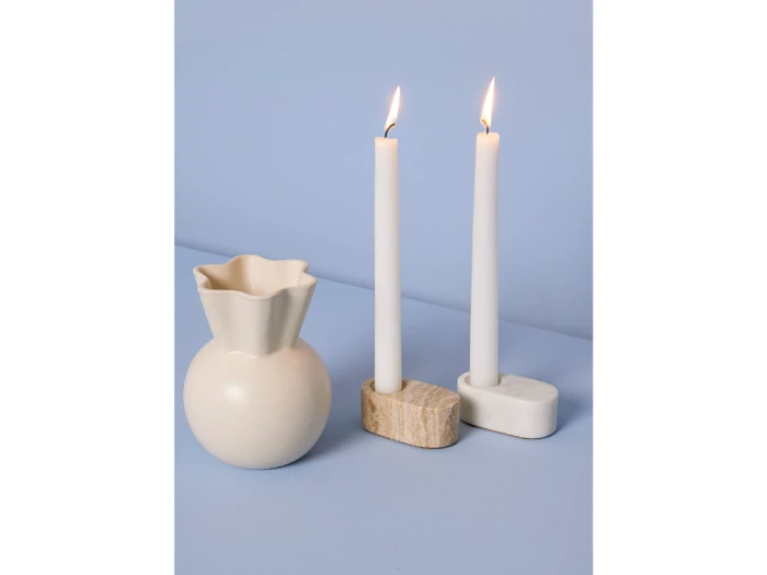 En cremefarvet vase og to tændte hvide lys i stenholdere står på en lyseblå baggrund.
