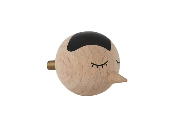Et rundt fuglehoved af træ med næb, lukkede øjne og en sort plet på toppen, set mod en almindelig hvid baggrund.