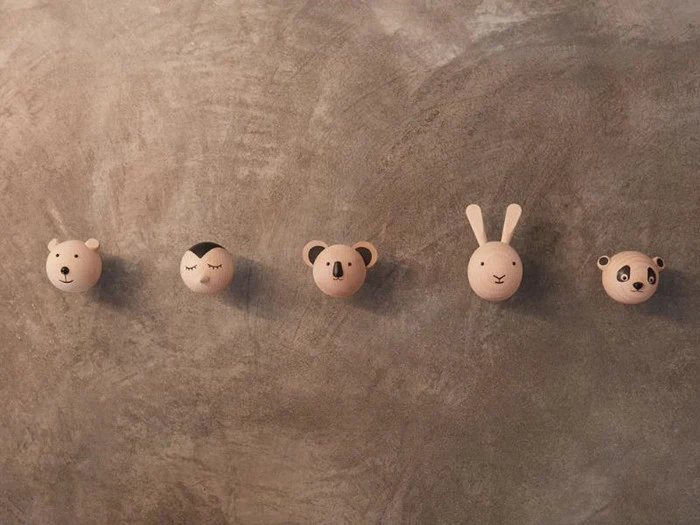 Fem runde vægkroge i træ formet som dyreansigter - bjørn, fugl, koala, kanin og panda - monteret på en struktureret grå væg.