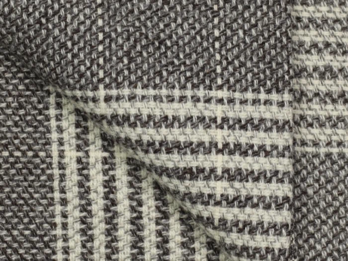 Nærbillede af foldet stof med et vævet mønster i sort, hvid og grå med vandrette og lodrette striber og en struktureret overflade.