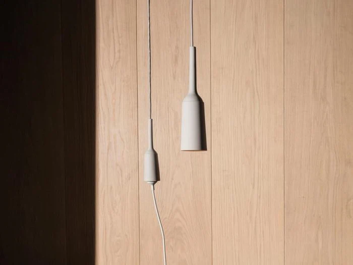 To minimalistiske hvide pendler hænger op ad en lys trævæg, hvor sollyset kaster en skygge på venstre side.