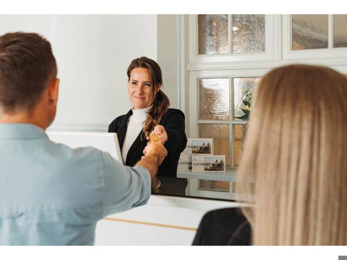 En receptionist giver en nøgle til en mand på den anden side af skranken, mens en kvinde står ved siden af ham i et lyst og indbydende receptionsområde.
