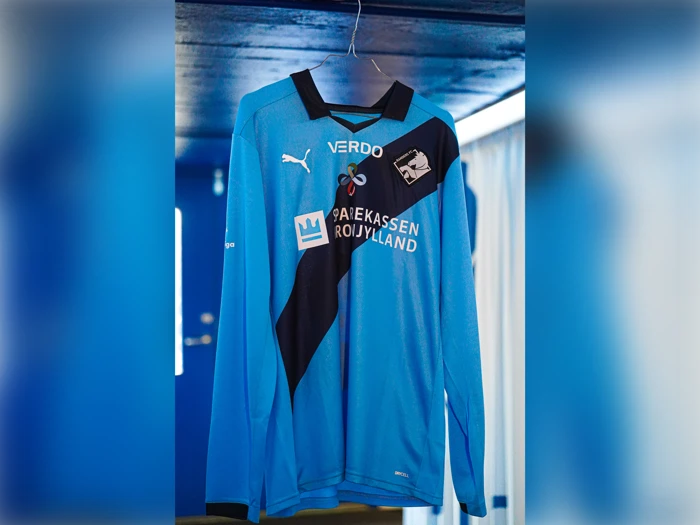 En langærmet, lyseblå Randers FC-fodboldtrøje med en sort diagonal stribe, sponsorlogoer og klublogo.
