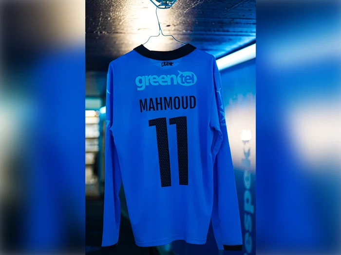 En lyseblå sportstrøje med lange ærmer, der hænger på en bøjle, med navnet MAHMOUD og nummeret 11 på ryggen.