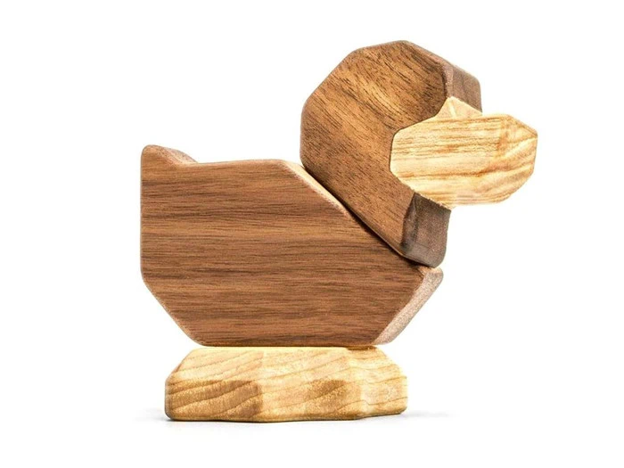 En legetøjsand i træ lavet af geometriske former med lyst næb og bund og en mørkere brun krop og hoved på en hvid baggrund.