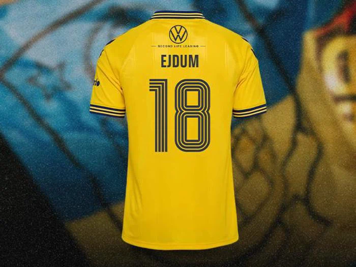 Bagside af en gul fodboldtrøje med Volkswagen-logoet, navnet EJDUM og tallet 18 i mørkeblå.