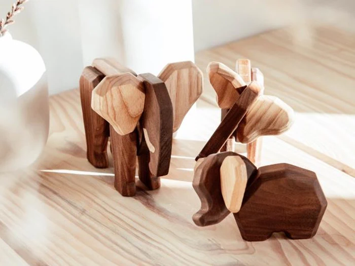 Tre elefantfigurer af træ i forskellige størrelser er udstillet på en træoverflade i naturligt sollys.