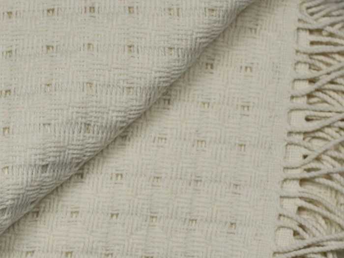 Nærbillede af et cremefarvet vævet tæppe med et geometrisk strukturmønster og frynsede kanter.